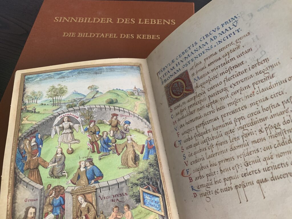 FBM23_23 Aufgeschlagene Fakisimile-Edition "Sinnbilder des Lebens - Die Bildtafel des Kebes". Die Seite zeigt den ersten Mauerring mit den personifizierten Gefahren, die das Leben mit sich bringt: u.a. Luxuria (die Wolllust), instabilitas (die Unbeständigkeit)